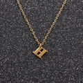 Macro view of gold stainless steel H letter pendant on a sparkling black background - Gold H