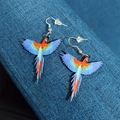 Close-up of laser-cut acrylic parrot earrings with vibrant blue and red feather details - Blue Macaw
