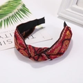 Close-up of red fabric knotted headband with intricate gold floral embroidery details - Red