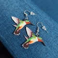 Colorful hummingbird acrylic drop earrings with silver hooks on dark fabric background - Colorful Hummingbird