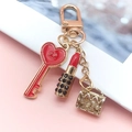 Detail of creative keychain with red heart, mini lipstick and golden handbag charms - Key + Lipstick + Bag