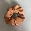 Dettaglio di un elastico per capelli in similpelle marrone su uno sfondo grigio neutro - Taglia Grande / Marrone