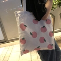 Close-up of white canvas tote bag with pink peach pattern worn by a model in outdoor setting - Apple