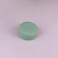 Macro detail of a mint green macaron shaped plastic container on a soft pink surface - 10 g / Dark Green