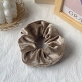 Elegant champagne velvet scrunchie hair tie on a white textured fabric background - Brown