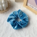 Glossy bright blue velvet scrunchie ponytail holder displayed on a white textured background - Teal