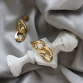 Détail de boucles d'oreilles géométriques dorées sur soie grise et décor en pierre - Doré