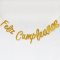Golden glitter Feliz Cumpleaños birthday banner hanging on a white brick wall background - Gold Glitter Spanish Birthday