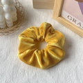 Vibrant yellow velvet scrunchie showing soft pleats on a minimalist white textured base - Gold Yellow