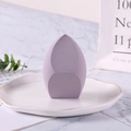 Esponja de maquillaje morada en forma de gota en un plato sobre fondo de mármol - Embalaje a granel / Morado