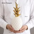 White ceramic pineapple decor with gold leaves being held to show 30cm size scale - 30X10cm / White