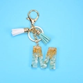 Detail view of resin letter M keychain with gold foil, blue stone and colorful tassels - M