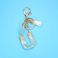 Detailed macro view of letter U resin keychain with gold foil, stones and blue tassels - Letter U