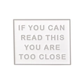 Macro detail of white enamel square badge with If You Can Read This text in grey - Square / White & Silver