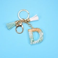 Detailed macro view of resin letter D keychain with gold foil, stones and mint tassels - Letter D