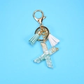 Close-up of resin letter X keychain with gold foil, light blue stones and colorful tassels - Letter X