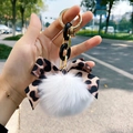 Close-up of leopard print bow and white faux fur pompom keychain with golden chain - White