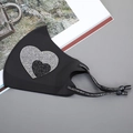 Detail der schwarzen Eisseidenmaske mit funkelndem Strass-Herz und bedruckten Ohrenschlaufen - Herz-Schwarz-Weiß