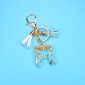 Detailed macro view of resin letter R keychain with green stones, gold foil and suede tassel - Letter R