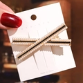 Macro shot of cross-shaped gold metal hair clip with white pearls and black center line - No.1 Pearl X-Shape Hair Clip