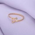 Detail van gouden letter U-ring met een kleine diamant op paarse getextureerde stof - Goud-U
