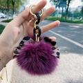 Close-up of a plush purple fox fur keychain with leopard print bow and gold chain links - Purple