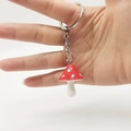Close-up of a red mushroom keychain with white spots held in hand on white background - Red