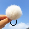 White faux fur pompom hair tie with elastic band shown against a blue sky background - White