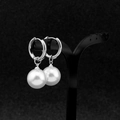 Detailopname van witte pareloorbellen aan een professionele zwarte sieradenhouder - Gepierceerde oorring / 14MM Parel Paar / Zilver/Wit