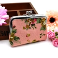 Close-up of floral canvas coin purse with vintage metal kiss-lock clasp on wooden box - Pink