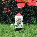 Wind-up snowman toy with red hat and green scarf on festive grass background - Head-shaking Snowman