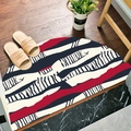 Semicircular entryway mat with red, black, and white abstract stripes on wood floor - British