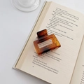 Square tortoise shell hair claw clip with dark brown amber gradient on an open book - Amber