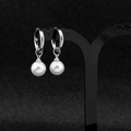 Macro-opname van zilveren oorringen met witte parels op een zwarte displaystandaard - Gepierceerde oorring / 10MM Parel Paar / Zilver/Wit