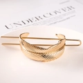 Detail showing the elegant golden metal feather hair pin on a minimalist white surface - Feather / Gold