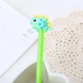 Simpatica penna gel dinosauro verde con topper in silicone in una tazza bianca - Verde
