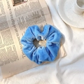 Elegant blue velvet scrunchie ponytail holder with soft texture on vintage newspaper - Blue