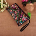 Close-up of black ethnic embroidered clutch bag with colorful floral patterns and green tassel - Butterfly