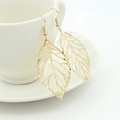 Fashionable golden leaf dangle earrings with leaf vein texture on a white cup edge - Gold