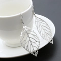Silver hollow leaf dangle earrings with clear vein texture hanging on a white ceramic cup - Silver