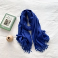 Blue cashmere-style fringed scarf laid flat on white fabric with decorative book and pot - Sapphire Blue