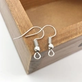 Detailed close-up of polished silver ear hooks on a wooden box for DIY jewelry making - 100 Pcs/Pack / White K/Silver