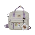 Detail of beige and purple canvas backpack featuring multiple pockets and cute badges - White