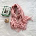 Pink cashmere-feel scarf with fringes on white fabric next to a green book - Sakura Pink