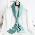 Elegant narrow green silk scarf for women shown tied on a white top with lifestyle props - Bean Green
