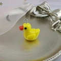 Close-up of a resin yellow duck pendant with a metal ring on a silver tray background - Yellow Duck