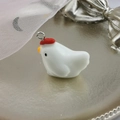 Macro shot of cute white resin chick pendant with red comb on a golden metal disk - Rooster