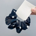 Detailed close-up of a black and white polka dot satin scrunchie held in hand - Black with White Polka Dots