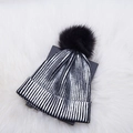 Detailed close-up of metallic silver striped knit beanie with large black faux fur pompom - One Size / Silver