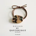 Elegant tortoiseshell acetate hair tie with gold trim on a soft leather surface - Brown